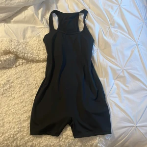 Svart oneshoulder bodysuit - Snygg svart oneshoulder bodysuit perfekt för träning eller en avslappnad dag. Den är ärmlös och har en tight passform som framhäver figuren. Materialet är mjukt och stretchigt för maximal komfort.