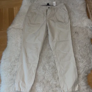 Beige byxor från H&M st.38 - Snygga beige byxor från H&M med knapp och dragkedja framtill. Perfekta för en avslappnad stil. De har en normal passform och är tillverkade i ett bekvämt material.