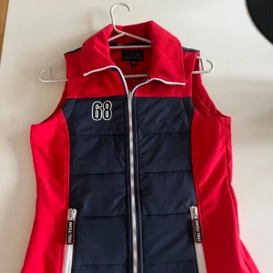 Röd och marinblå väst från Pro-Team - Säljer en snygg röd och marinblå väst från Pro-Team med dragkedja och nummerdetalj på framsidan. Perfekt för ridning med texten 'Riding Experts' på baksidan. Västen har en sportig look och är idealisk för aktiva dagar. Aldrig använd bara testad o jag är 170 lång och den passar fortfarande! 200kr+ frakt (nypris 479kr) 2 Små fläckar vid dragkedjan på utsida ficka men ingen man tänker på!