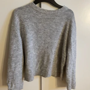 Grå stickad tröja - Mysig grå stickad tröja med rund hals och långa ärmar. Perfekt för kyligare dagar och enkel att matcha med olika outfits.