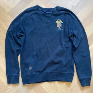 Navy sweatshirt från morris - Säljer en navy sweatshirt från Morris med ett broderat emblem på bröstet. Tröjan har långa ärmar och ribbade muddar vid ärmslut. Skriv vid fler frågor eller pris. 