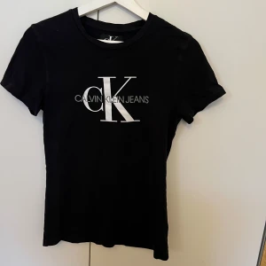 Svart t-shirt från Calvin Klein Jeans - Snygg svart t-shirt från Calvin Klein Jeans med stort vitt CK-logotryck på framsidan. Perfekt för en stilren och avslappnad look. Kortärmad och tillverkad i mjukt material för extra komfort.