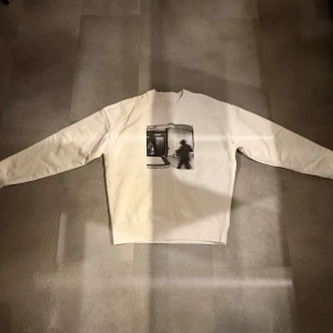 Merchsweden break in tröja  - Säljer en vit sweatshirt från Merchsweden med ett unikt tryck på framsidan som föreställer en övervakningsbild. Baksidan har en tryckt tidslinje med händelser. Tröjan har långa ärmar och en rund halsringning. Helt oanvänd och limiterad. Passar både S OCH M