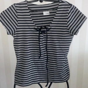 Randig träning topp från Casall st. M - Snygg svart och vit randig topp från Casall med korta ärmar och knytning framtill. Perfekt för en avslappnad stil.