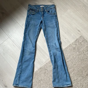 Blå jeans från Gina Tricot🩵 - Snygga blå jeans från Gina Tricot i en klassisk bootcut-stil. De har en lågmidjad passform och är perfekta för en avslappnad look. Jeansen har fickor både fram och bak samt en dragkedja med knapp framtill.