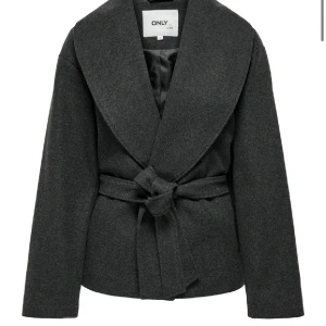 Mörkgrå kavaj från ONLY - Snygg mörkgrå kavaj från ONLY med bred krage och knytband i midjan. Perfekt för en stilren look. Kavajen har långa ärmar och en elegant design.