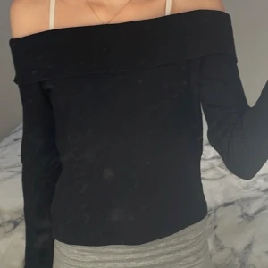 Svart offshoulder topp från H&M - Säljer en stilren svart offshoulder topp från H&M. Toppen är ribbad och har långa ärmar, perfekt för en trendig look. Passar både till jeans och kjol. Hör av dig vid intresse!