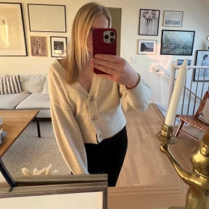 Beige kofta med dekorativa knappar - Säljer en mysig beige kofta med dekorativa knappar. Koftan har en ribbad struktur och långa ärmar, perfekt för kyligare dagar. Den är både stilren och bekväm, vilket gör den till ett mångsidigt plagg i garderoben.