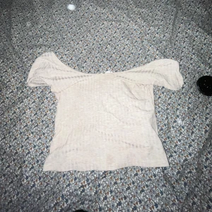 Beige offshoulder topp - Säljer en stilren beige offshoulder topp. Perfekt för en avslappnad och trendig look. Toppen har en mjuk och bekväm passform.
