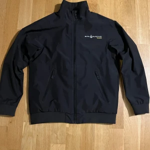 Svart jacka från Sail Racing - Säljer en svart jacka från Sail Racing med GORE-TEX-material som håller dig torr. Jackan har dragkedja framtill och broderad logga på bröstet och är i nyskick. Perfekt för blåsiga dagar med sin stilrena design och funktionella detaljer. Passade mig tills jag var ca 160cm