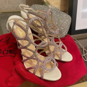 Glittriga klackskor från Louboutin - Snygga glittriga klackskor från Louboutin med öppen tå och remmar. Skorna har en elegant design med hög klack och justerbar rem runt ankeln. Perfekta för att ge en glamorös touch till din outfit.