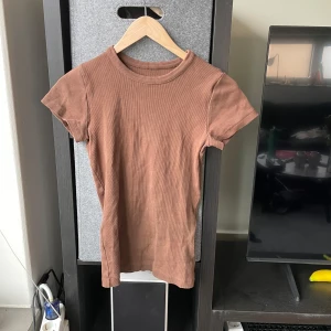 Brun ribbad topp från Djerf avenue - Säljer en snygg brun ribbad topp från Djerf avenue. Den har korta ärmar och en rund halsringning. Perfekt för en stilren look. Passar bra till både jeans och kjol.
