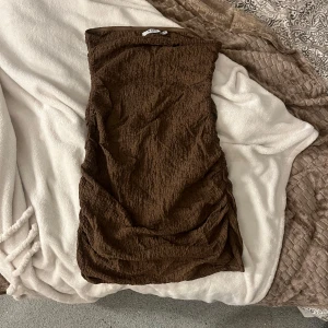 Brun klänning från NA-KD - Snygg brun klänning från NA-KD i en skön, texturerad design. Perfekt för att sticka ut med sin unika stil. Klänningen är ärmlös och har en tight passform som framhäver figuren. Ett måste i garderoben för den modemedvetna!