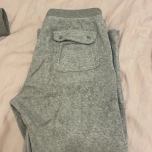 Grå mjukisbyxor med fickdetalj - Säljer ett par grå mjukisbyxor med en praktisk ficka med knappdetalj på baksidan. Byxorna har en bekväm passform och är perfekta för en avslappnad stil. Pris går att prata om!