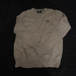 Beige tröja från Lyle & Scott - Säljer en stilren beige tröja från Lyle & Scott med deras ikoniska logga på bröstet. Tröjan är långärmad och har ribbade muddar vid ärmslut och nederkant. Perfekt för en avslappnad och snygg look.