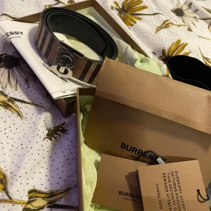 Äkta Burberry bälte med alla tillbehör  - Säljer ett stilrent bälte från Burberry med klassiskt rutigt mönster och ett elegant spänne i silver. Perfekt för att ge en touch av lyx till din outfit. Kommer i originalförpackning med alla tillbehör, nypris 4200kr