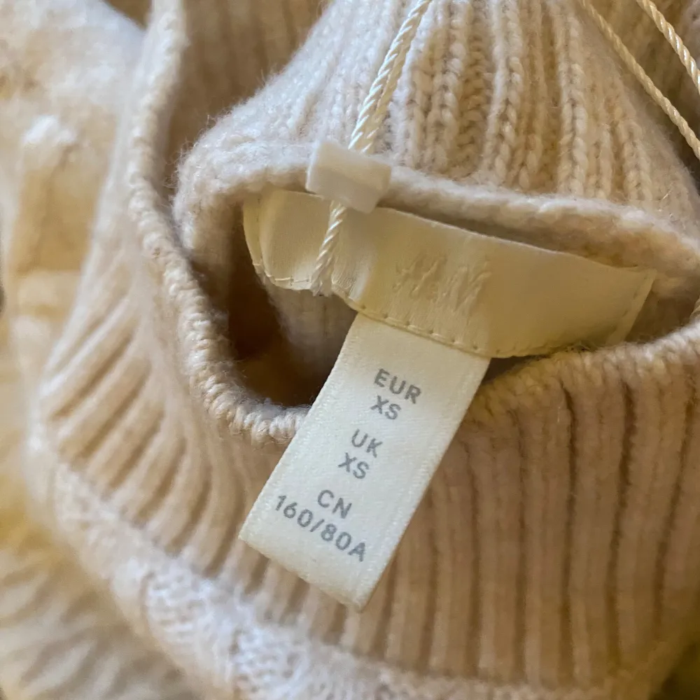 Säljer en mysig vit stickad klänninh från H&M med ett snyggt flätmönster. Tröjan har långa ärmar och en hög krage. Perfekt för kyliga dagar! Den är oversize och skulle säga att den passar xs-m. Mekot.