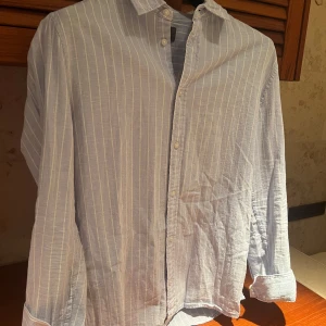 Randig linnéskjorta från H&M - Snygg ljusblå skjorta från H&M med vita ränder. Skjortan har en slim fit passform och långa ärmar. Linnéblandning vilket gör den perfekt för sommaren!