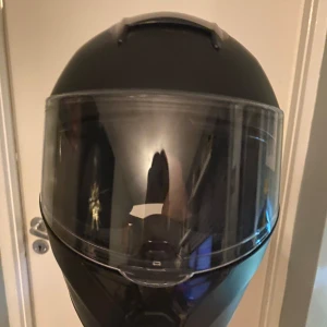 Svart hjälm från BNO - Säljer en svart motorcykelhjälm från BNO med visir. Hjälmen har en slät och stilren design med en tydlig logotyp på baksidan. Perfekt för säker körning. Storlek är 56-58 cm runt huvudet 