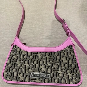 Axelväska från Acne Studios - Snygg axelväska från Acne Studios med ett unikt mönster i svart och beige. Väskan har rosa läderdetaljer och en justerbar axelrem. Perfekt för att ge din outfit en färgklick! Aldrig använd, köpt på deras rea för strax under 6000kr men glömde skicka tillbaka den. Kommer med dustbag.