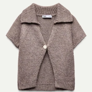 Beige stickad kofta från Zara - Säljer en stilren beige stickad kofta från Zara med korta ärmar och en stor knapp framtill. Perfekt för lager-på-lager under kyligare dagar. Den har en ribbad krage och nederkant för extra stilpoäng.