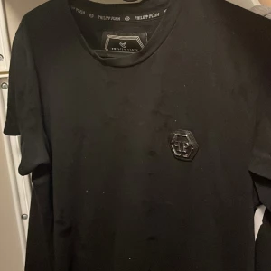 Svart t-shirt från Philipp Plein - Snygg svart t-shirt från Philipp Plein med en cool logotypdetalj på bröstet. T-shirten har en klassisk passform och är perfekt för en stilren look. Tillverkad i ett mjukt material för extra komfort.