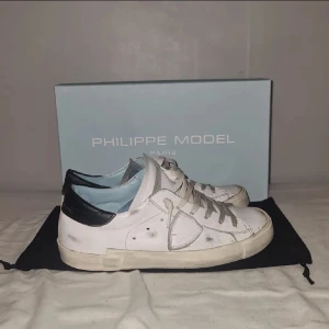 Vita sneakers från Philippe Model - Jag säljer mina vita snygga Philippe Model med svarta detaljer och snörning. Jag säljer de på grund av att det har blivit försmå för mig då jag tycker det är bättre och sälja dom än att bara låta dom så hemma, kvitto kan jag nog leta fram om de önskas och box+påse är med. Hör av dig om du har frågor. 