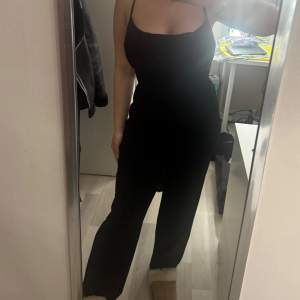 Snygg svart jumpsuit med smala axelband och korsad ryggdesign. Perfekt för en stilren look. Den har en tight passform upptill och vida ben som ger en elegant siluett.