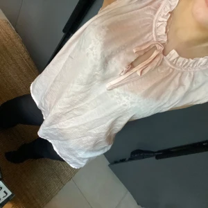 Ljusrosa ärmlös blus / topp - Säljer en söt ljusrosa ärmlös blus med knytband vid halsen. Blusen har en lätt och luftig design, perfekt för varmare dagar. Den har en volangdetalj runt halsringningen 💕💕