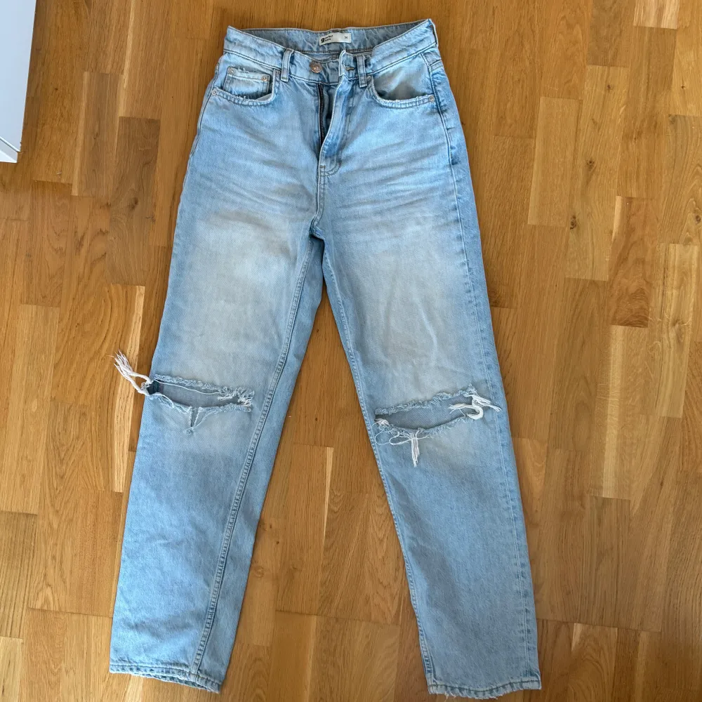 Säljer ett par ljusa jeans med coola slitningar på knäna. De har en hög midja och en straight passform som ger en avslappnad look. Perfekta för en casual outfit!. Jeans & Byxor.