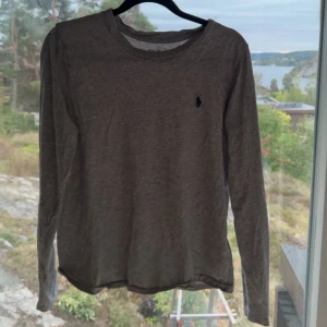 Grå långärmad tröja från Ralph Lauren - Säljer en stilren och bekväm grå långärmad tröja från Ralph Lauren. Tröjan har en klassisk design med en liten broderad logga på bröstet. Perfekt för både vardag och lite finare tillfällen. Passar bra till jeans eller chinos!