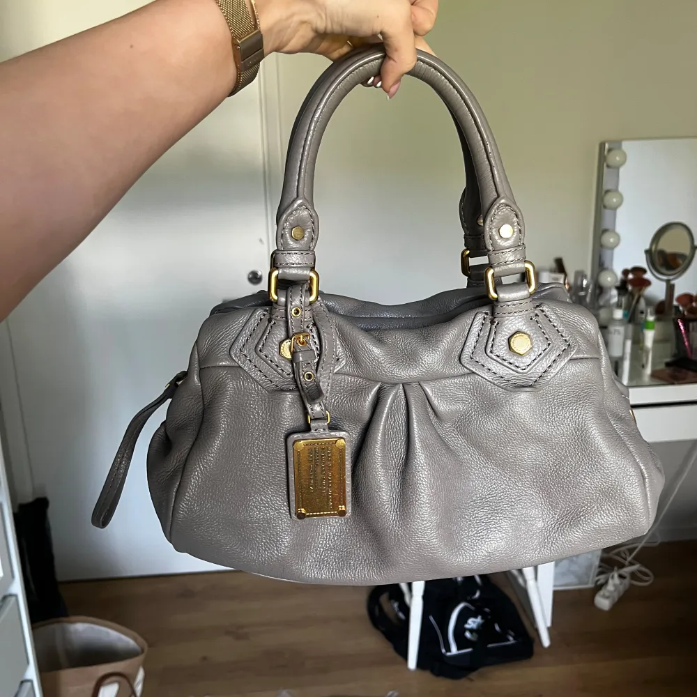 Marc Jacobs classic q baby groove med guldiga detaljer. Väskan är i en grå/beige färg. Axelremband ingår. Den är ca 30 cm bred och är i den lilla modellen. Väldigt bra skick. Fler bilder finns och svarar gärna på frågor 🩶. Väskor.