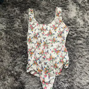 Säljer en superfin blommig baddräkt från Beach Wear by Hennes & Mauritz. Den har ett färgglatt blommönster på en vit bakgrund och breda axelband. Perfekt för sommarens stranddagar! 🌸