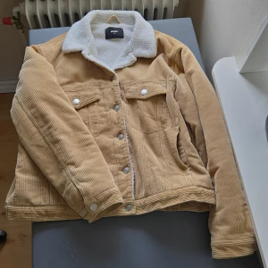 Beige manchesterjacka från Bik Bok - Säljer en snygg beige manchesterjacka från Bik Bok i storlek XL. Jackan har en mysig vit teddykrage och knappar framtill. Perfekt för höst och vår med sin stilrena design och bekväma passform. Jackan har två bröstfickor med knappar och är tillverkad i 100% bomull.