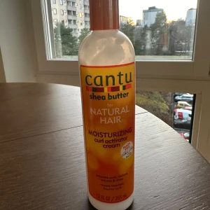 Cantu Shea Butter Moisturizing Curl Activator Cream - Cantu Shea Butter Moisturizing Curl Activator Cream för naturligt hår. Denna kräm återfuktar och definierar lockar med sheasmör och naturliga oljor. Perfekt för att ge liv åt trötta lockar och minska friss. Mer än hälften kvar. 