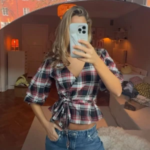 Rutig omlottblus - Säljer en snygg rutig omlottblus med knyt i midjan. Blusen har trekvartsärmar och en v-ringad design. Storlek S/M