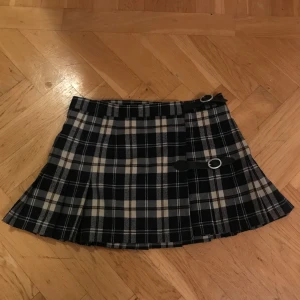 Rutig kortkjol Brandy Melville  - Snygg rutig kortkjol i marinblått och vitt med två dekorativa spännen i midjan. Perfekt för en trendig look. Vafan är lite nopprig men annars i bra skick se bild 2 