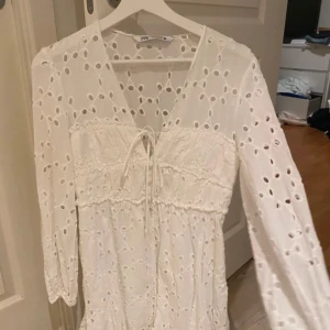 Studentklänning  - Vit klänning från Zara med broderade detaljer och v-ringning. Klänningen har långa ärmar och en knytning framtill.  Storlek M men är liten i storleken så passar mer S. 