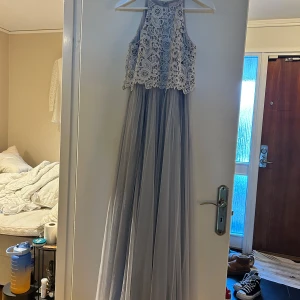 Grå långklänning med spetsdetaljer från Eve - Elegant grå långklänning från Eve med vacker spetsöverdel och flytande kjol. Perfekt för speciella tillfällen med sin sofistikerade design och detaljerade spetsmönster.