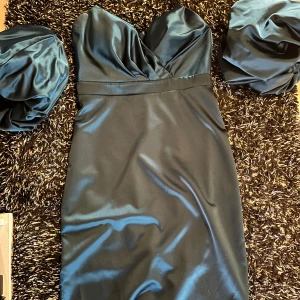 Grön axelbandslös klänning - Snygg svart axelbandslös klänning i satin med en elegant passform. Perfekt för festliga tillfällen. Klänningen har en vacker struktur och en stilren design som framhäver figuren.