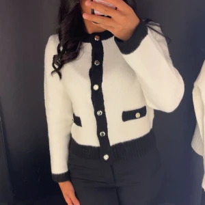 Vit och svart kofta med knappar - Säljer en snygg vit kofta med svarta detaljer och guldknappar. Har endast använts 2 gånger. Perfekt till vardags eller fest. Nypris 299.