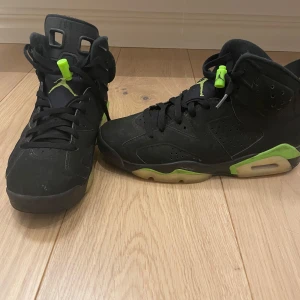 Svarta Nike Air Jordans 6  - Snygga svarta Nike Air Jordans med gröna detaljer och snörning. Perfekta för dig som vill ha en stilren och sportig look. Sulan har en cool design med gröna inslag. Köpt från JD.
