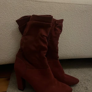 Vinröda mockastövletter med dragkedja - Snygga vinröda stövletter i mocka med dragkedja på sidan. De har en medelhög klack och en rynkad design upptill som ger en trendig look. Super snygga! 