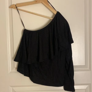 Svart oneshoulder topp med volang - Snygg svart oneshoulder topp med volang, glittrigt tyg!