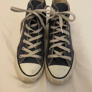 Blå Converse - Säljer ett par klassiska blå Converse All Star sneakers i bra skick. De har en hög modell med snörning och loggan på sidan. De är slitna och smutsiga därav priset men kan nog lätt fixas om man tvättar de🥰