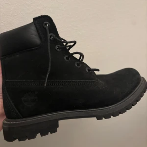 Svarta boots från Timberland - Säljer ett par svarta Timberland boots i bra skick. De är gjorda av mocka och har en robust sula perfekt för höst och vinter. Skorna har snörning och en bekväm vadderad krage. Använda endast ett fåtal gånger, och fläckarna är förmodligen från snö/slask, vet ej om det går att få bort. Tycker det är synd att dem inte används och vill därför sälja dem. Betalade cirka 2000kr för dem