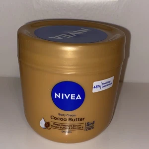 Helt ny  - NIVEA Body Cream Cocoa Butter med djup återfuktning och vitamin E. Perfekt för torr hud med 48 timmars vård. Kommer i en guldbrun burk.