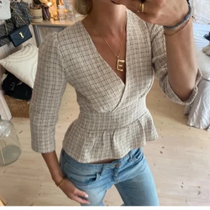 Beige rutig blus med v-ringning - Säljer en elegant beige blus med rutigt mönster och v-ringning. Blusen har trekvartsärmar och en peplumdetalj i midjan som ger en smickrande silhuett. Perfekt för en stilren look. (De två första bilderna är lånade från förra ägaren)