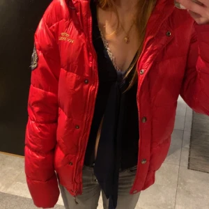 Röd dunjacka från HV Polo Ralph Laurent - Snygg röd dunjacka från HV Polo med broderad logga på bröstet. Jackan har en praktisk dragkedja och knappar framtill samt en mysig huva. Perfekt för kyliga dagar. Vinterjacka 💕☃️storleken är i barn så den motsvarar xs/s