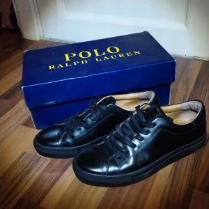 Svarta sneakers från Polo Ralph Lauren - Snygga svarta sneakers från Polo Ralph Lauren i skinn. Skorna har en klassisk design med snörning och en bekväm innersula. Perfekta för en stilren look.